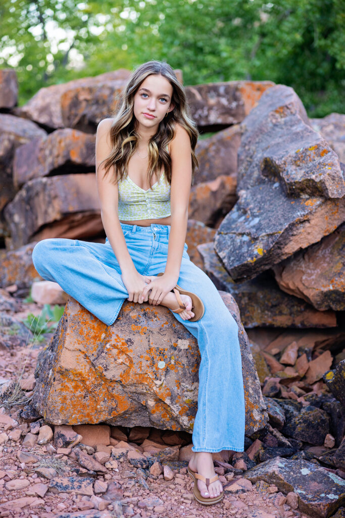 High school senior girl sitting on a rust-colored rock with soft curls and casual jeans – outdoor senior photos in Northern Colorado.