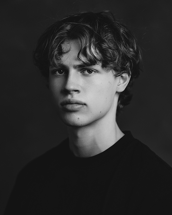 Fine art black and white headshot of teen boy with moody expression – classic studio senior portrait.