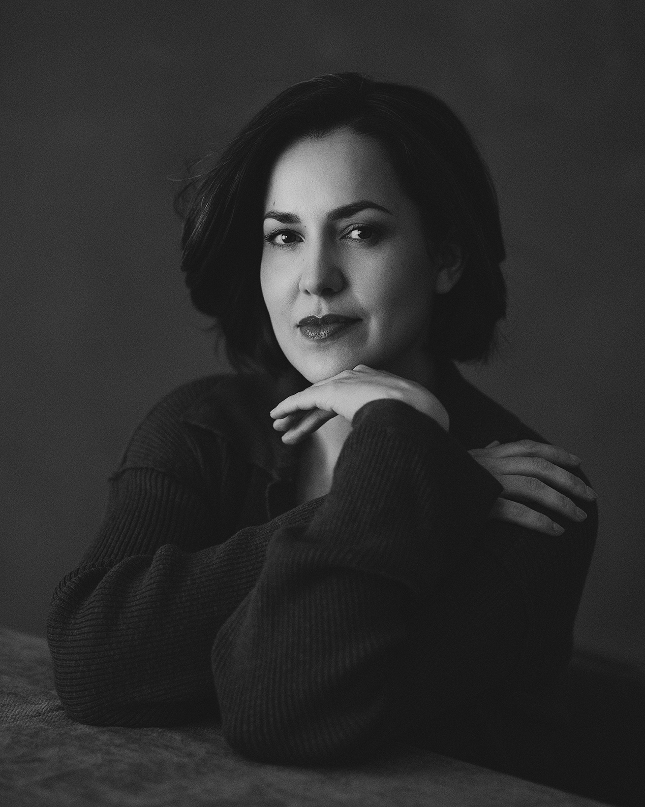 Studio portrait of woman with folded arms and soft smile in black and white