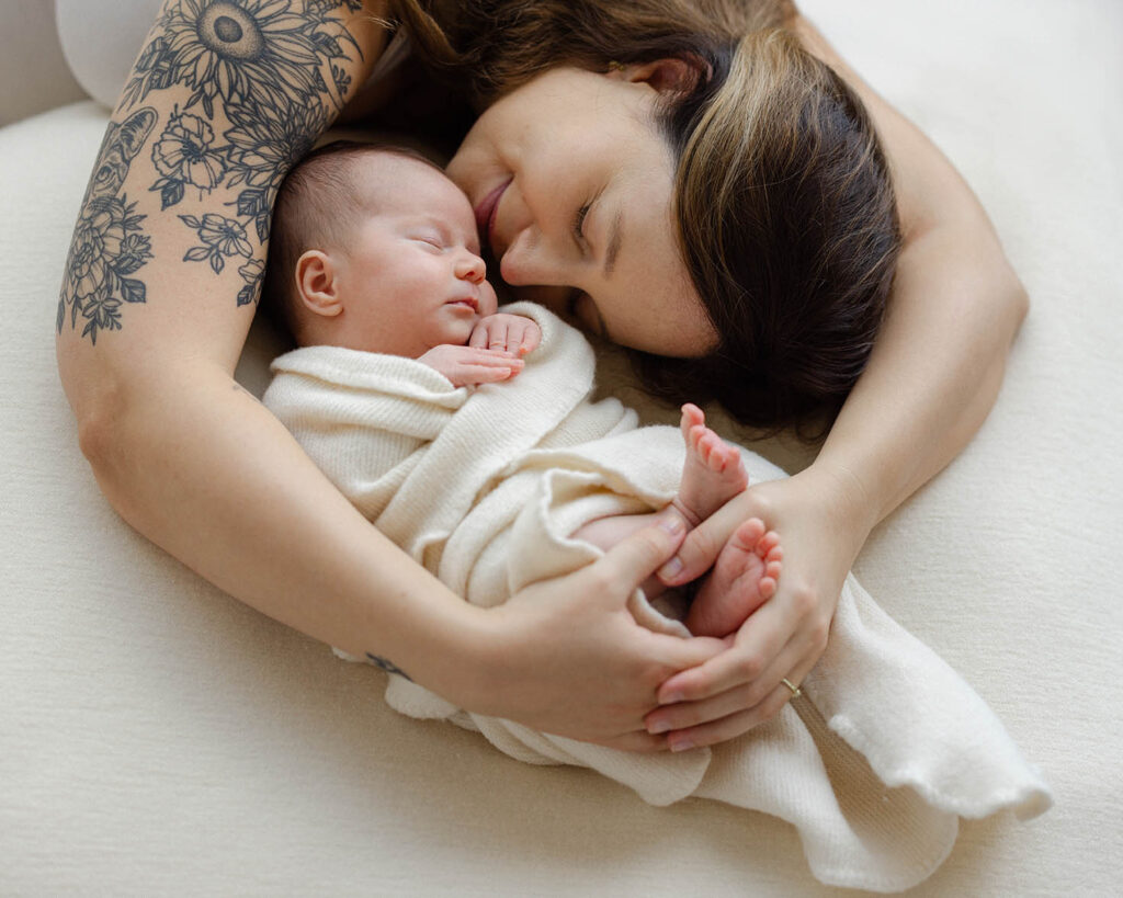 “Mom tenderly holding her newborn wrapped in a cream swaddle during a natural newborn photo session in Fort Collins.”