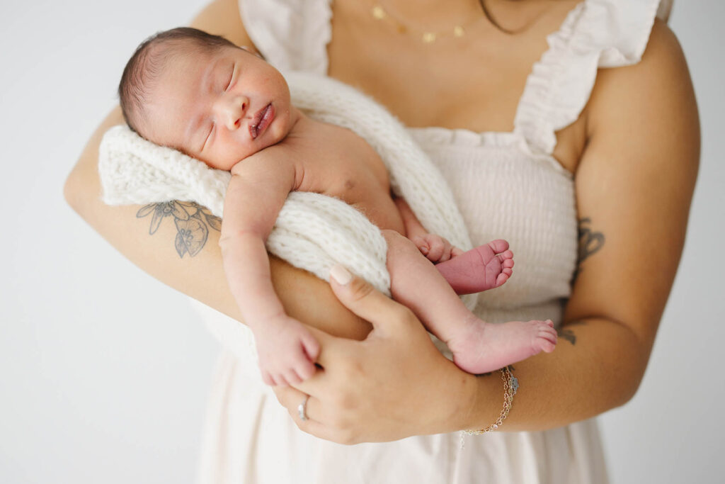 “Mother holding newborn wrapped in cream knit blanket during a baby-led photography session in Fort Collins.”