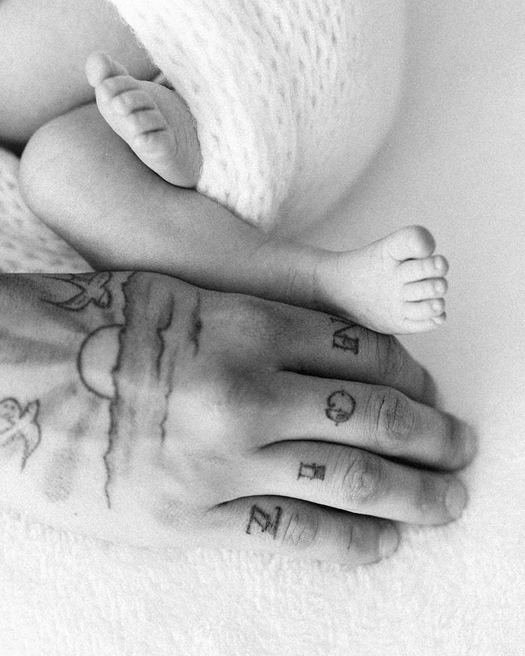 detail shot of dad's hand next to newborn baby foot