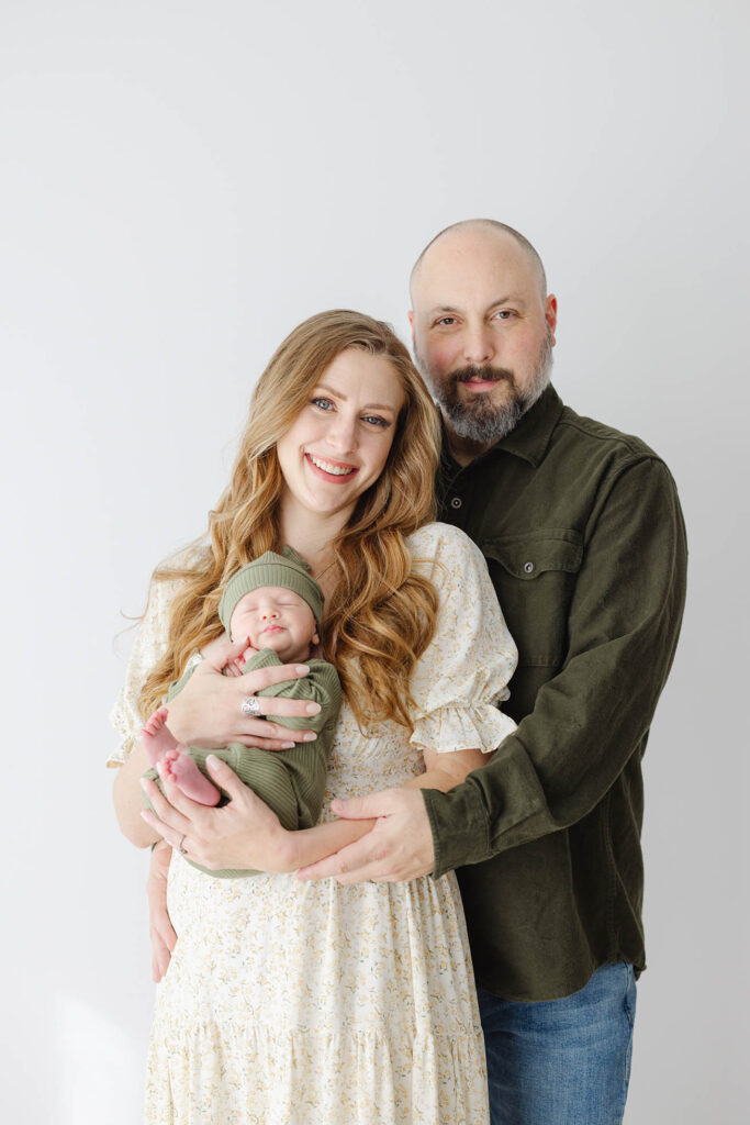 two parents standing and posing with newborn baby