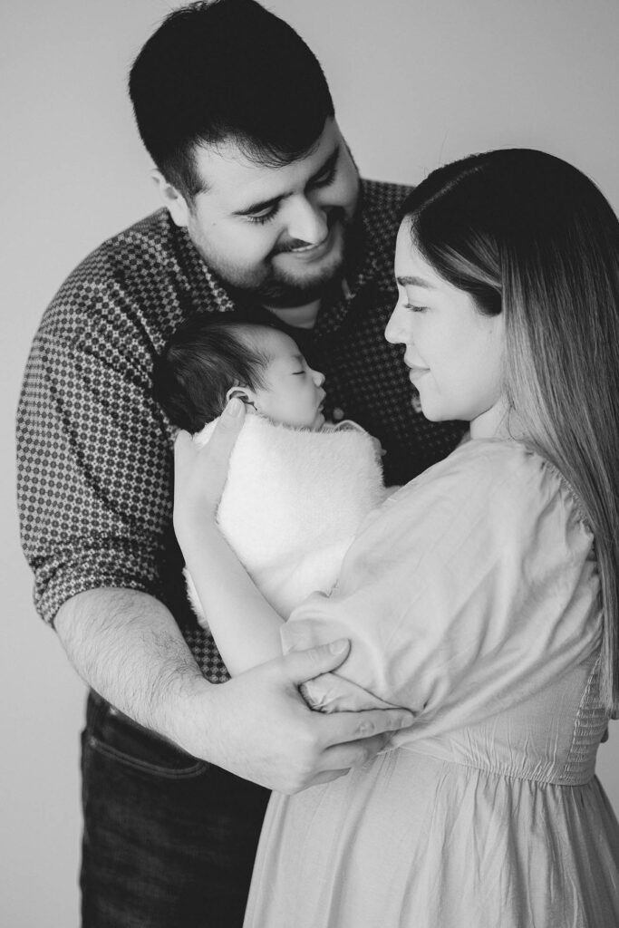 two new parents holding newborn baby while dad gazes lovingly at mom