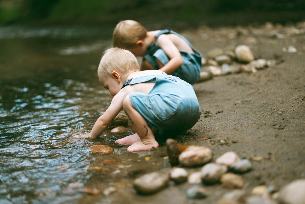 two boys playing with rocks along river
