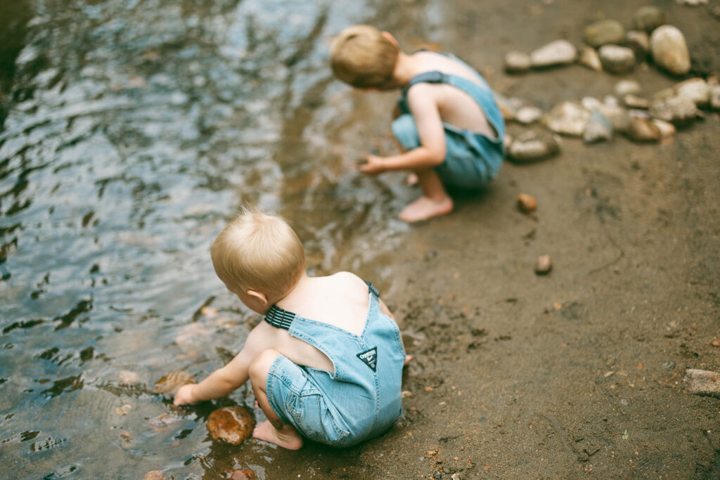 two boys in summer playing with rocks along calm stream