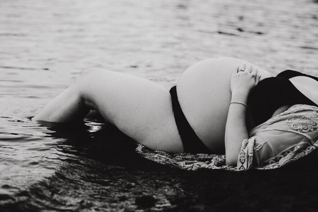 photo of pregnant woman's belly as she lays on the shore of a lake