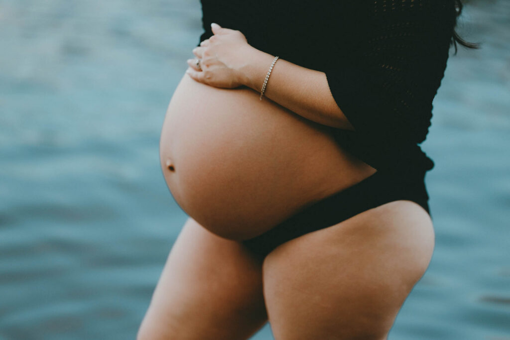close-up shot of pregnant belly with blue lake in background