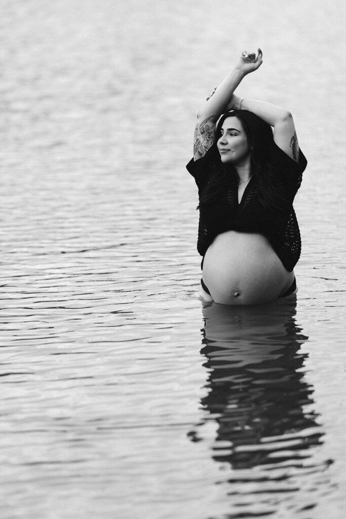 maternity photo of woman in lake with arms overhead