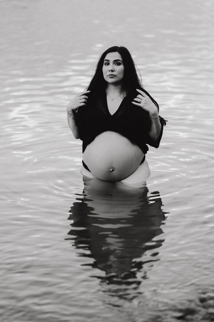 Maternity phot of woman standing in lake gazing at camera