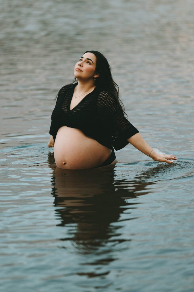 photo of pregnant woman standing in lake stroking the top of the lake with her hands and gazing up