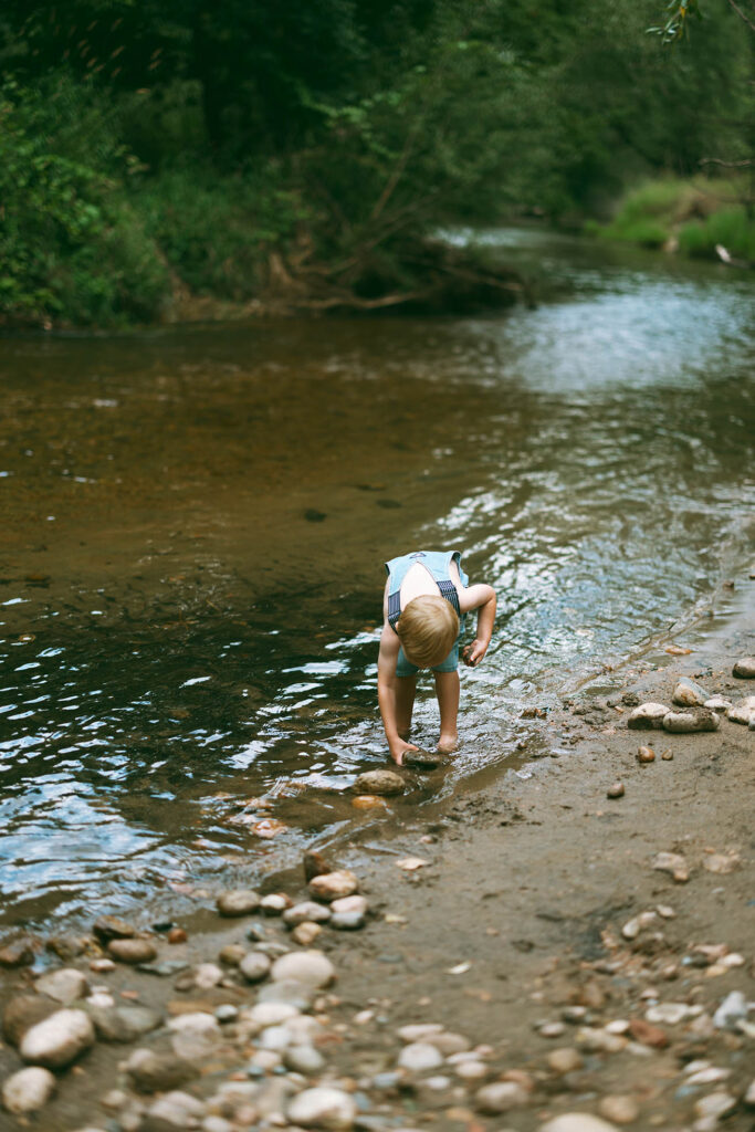 boy picking up a rock from stream in summer