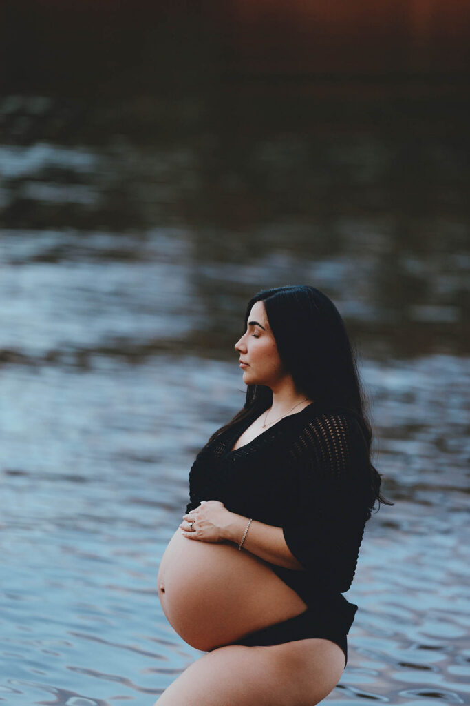 photo of pregnant standing in lake in bikini bottom and top with her eyes closed