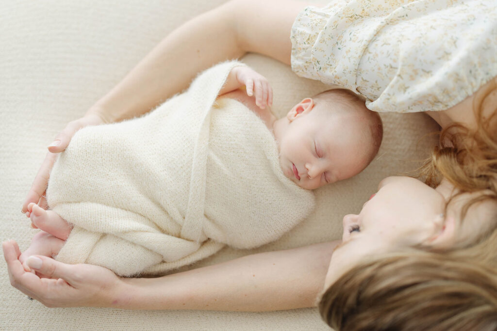 photo of mother laying with newborn baby with arms wrapped around baby