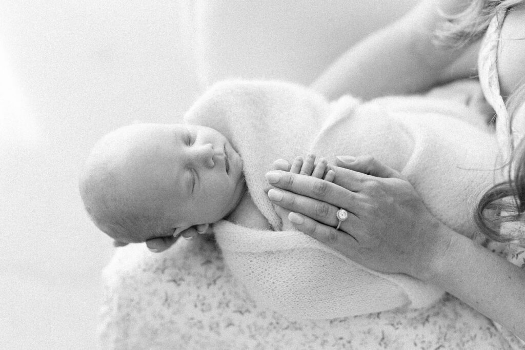 closeup photo of newborn baby on mothers lap with his fingers in her fingers