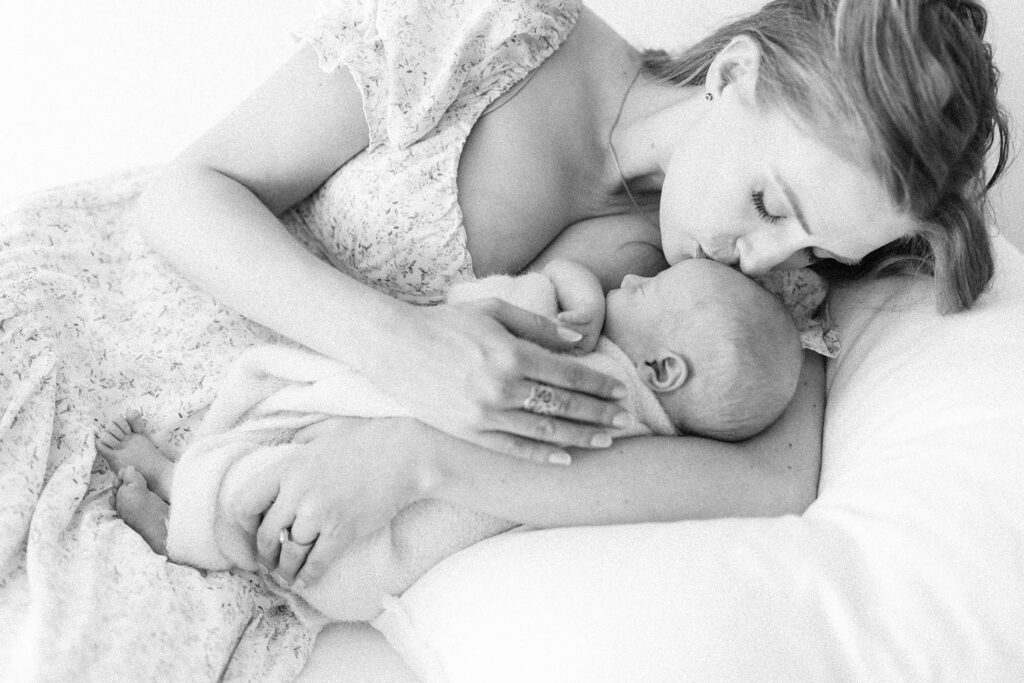 photo of mother laying next to newborn bay and kissing him on the head
