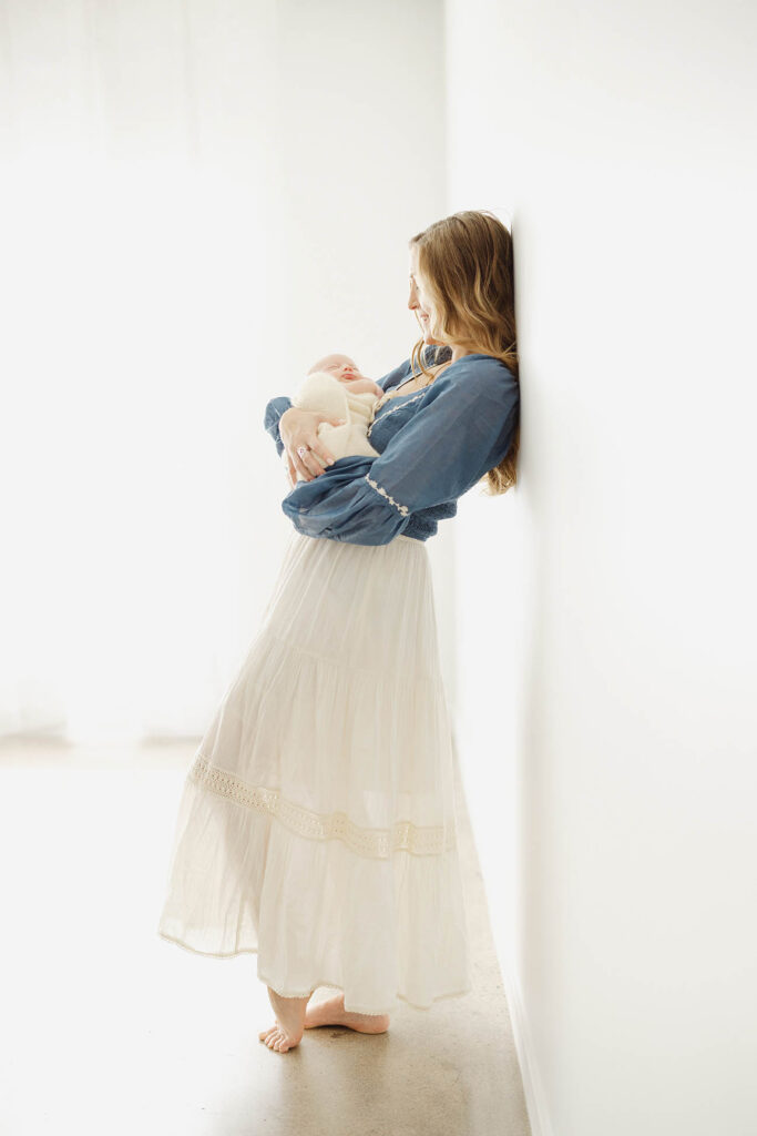 full length photo of mother holding newborn baby in glowy light