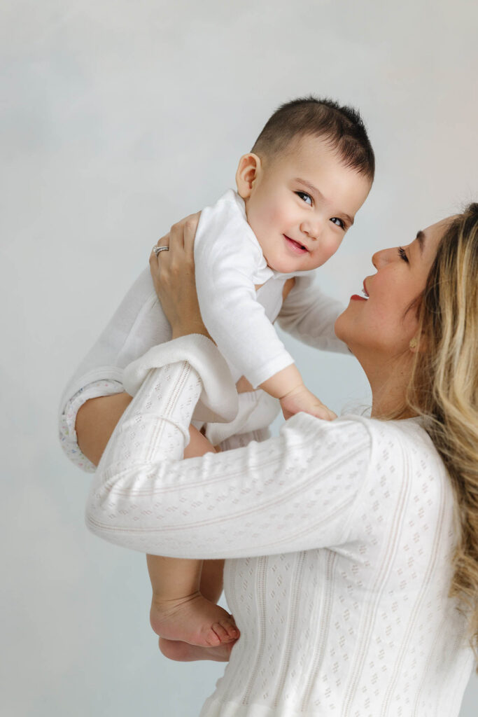 mother lifting baby and smiling during studio milestone session