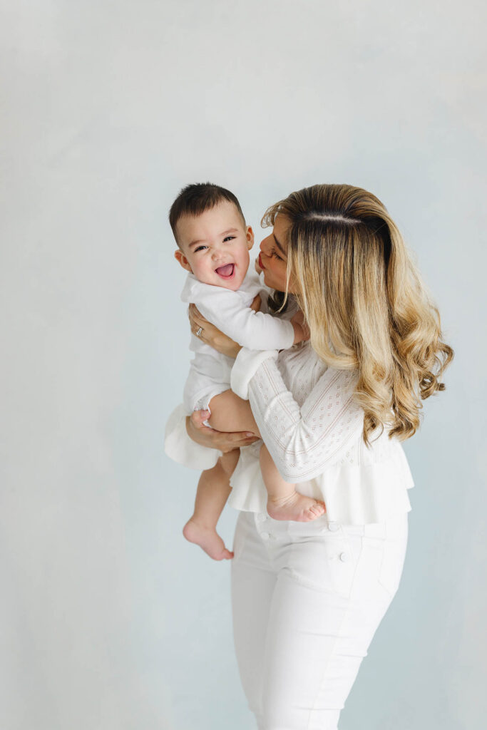 mother kissing smiling baby during milestone session