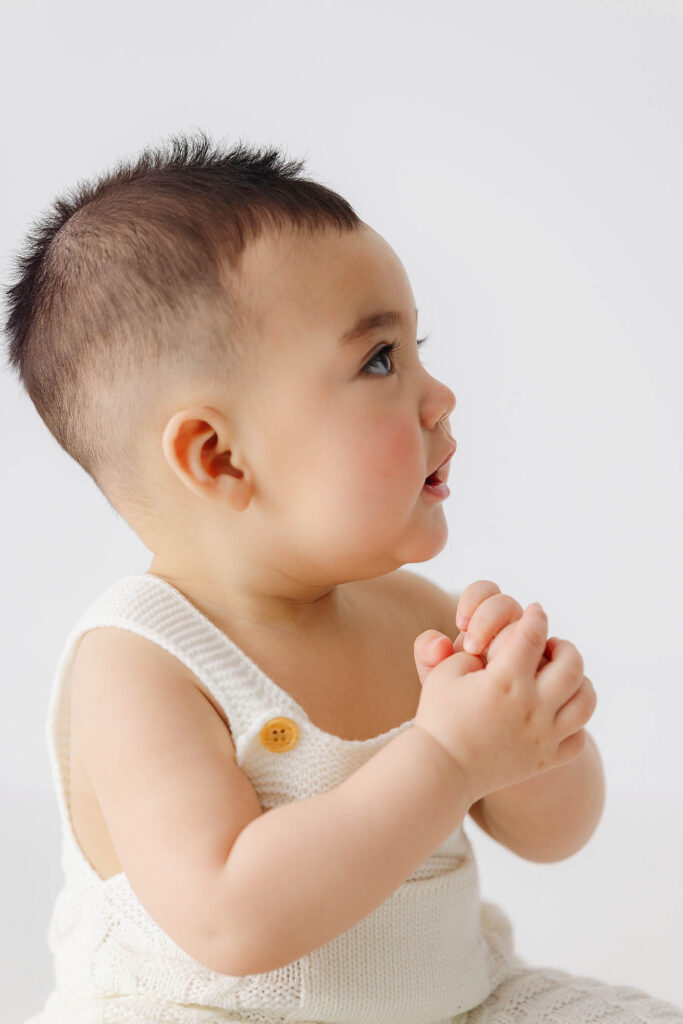 side profile of 6 month baby with hands together during sitter milestone session in studio
