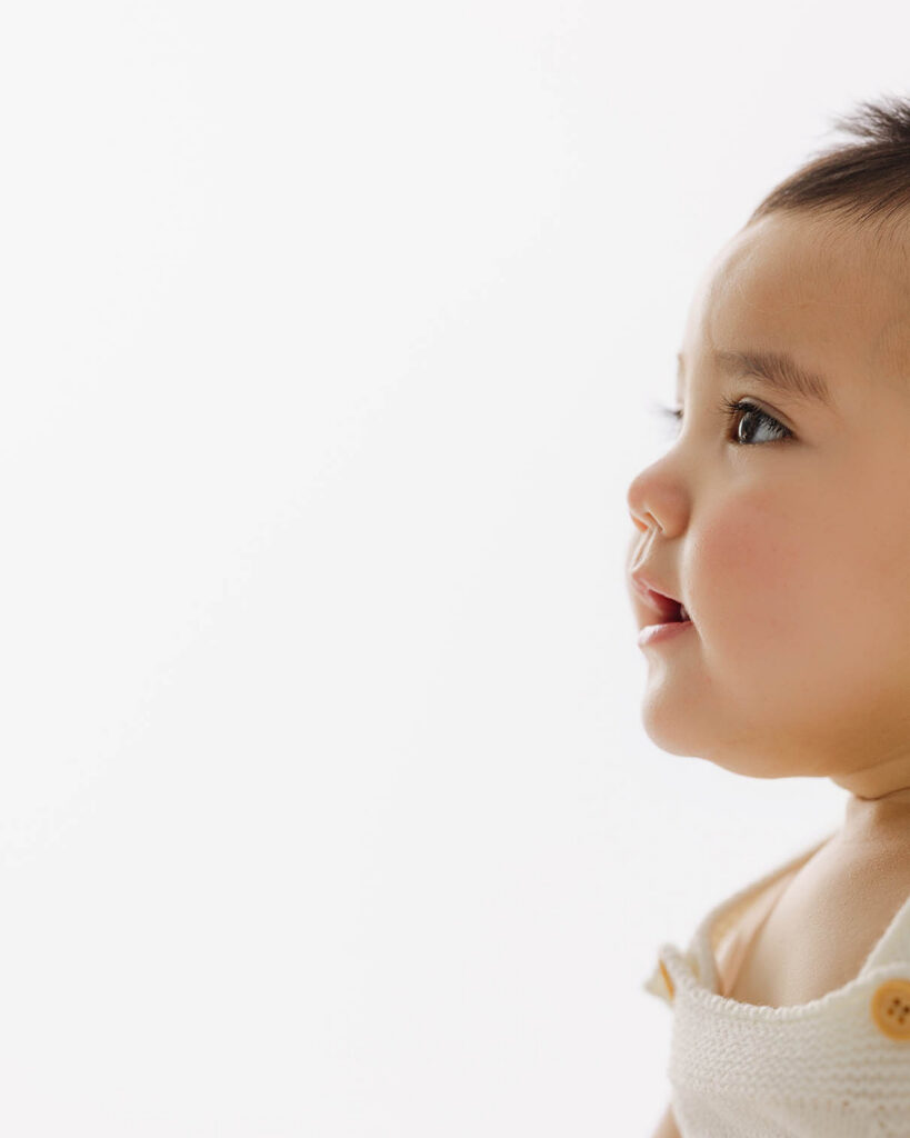 side profile of baby looking forward with soft light during milestone session in neutral studio