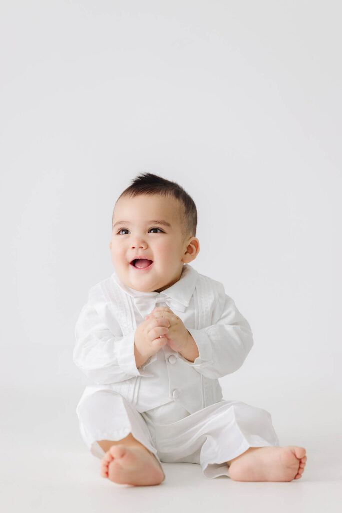 6 month baby sitting in white outfit smiling during milestone photos in Fort Collins studio