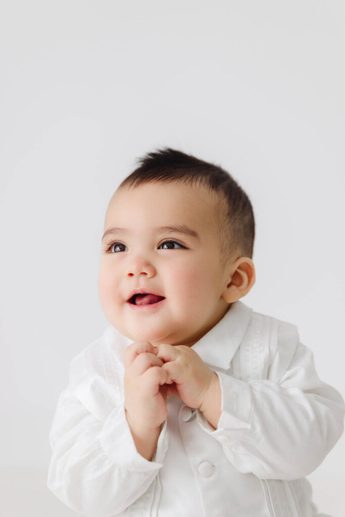 smiling 6 month baby with hands together during sitter milestone session in studio