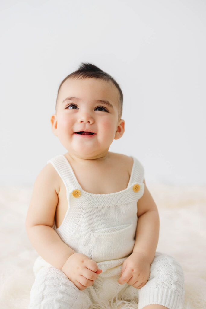 smiling 6 month baby sitting upright in neutral studio setting during baby milestone session