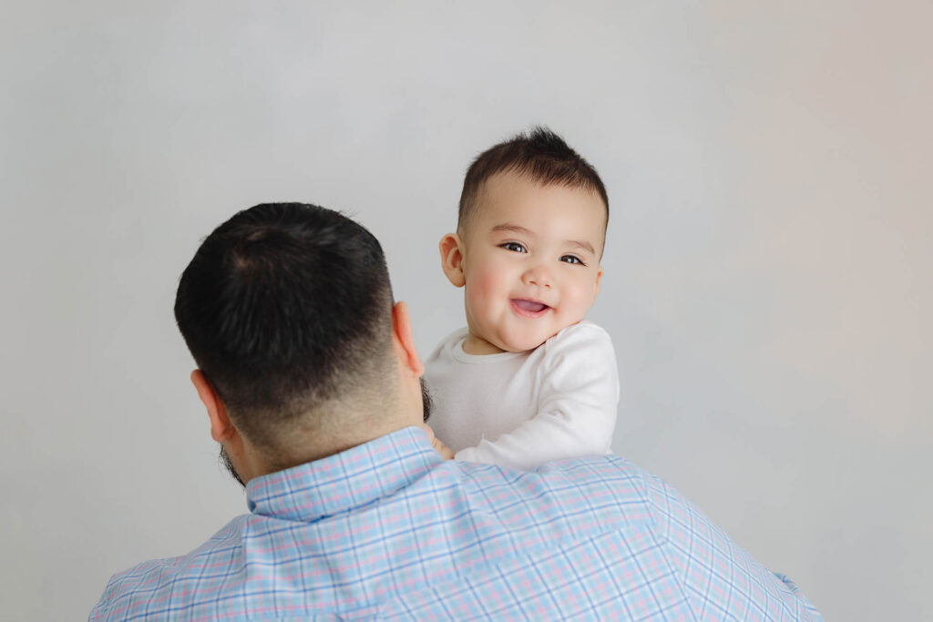 baby smiling over father’s shoulder during studio milestone session