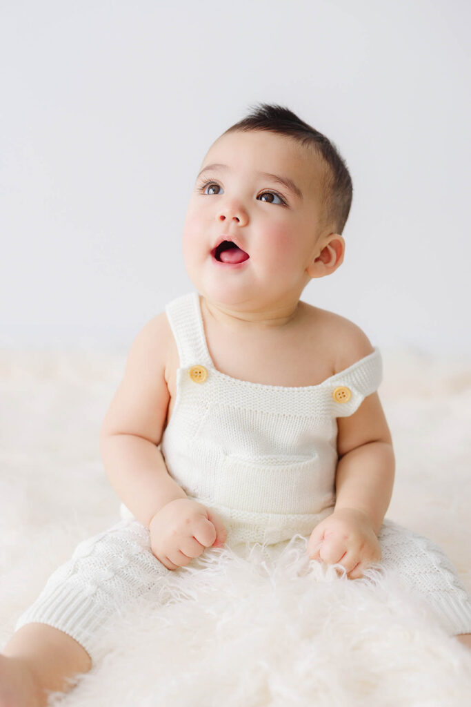 6 month baby sitting in studio looking up with open mouth during milestone photos