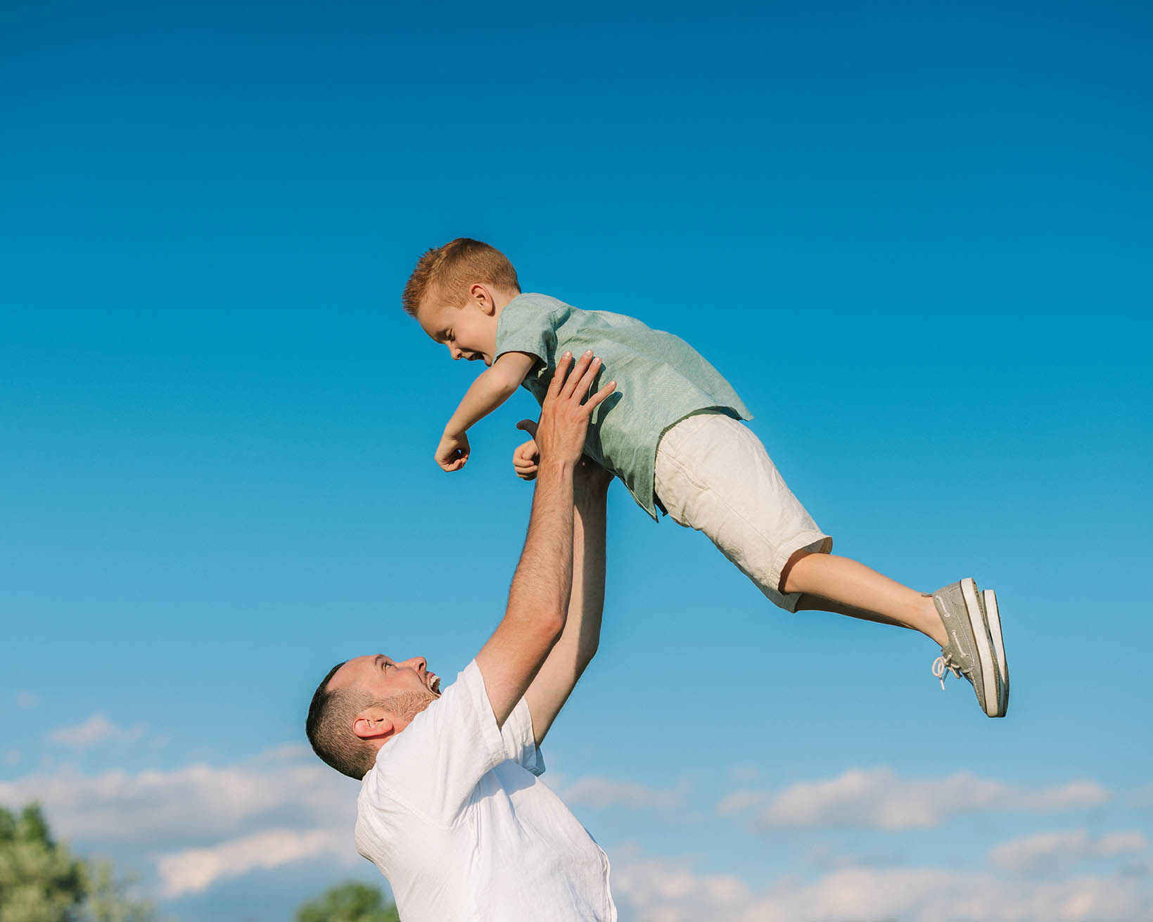 Dad throwing boy into air and cathcing him with deep blue sky in the background