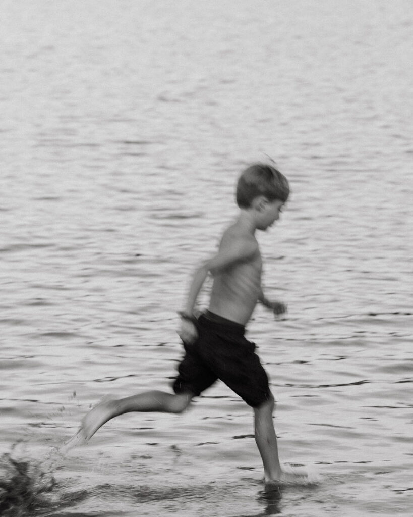 photo of boy running through lakeside water