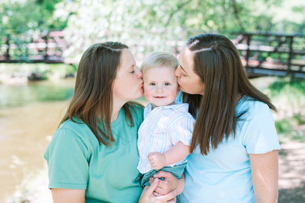 two mothers kissing their baby held between them