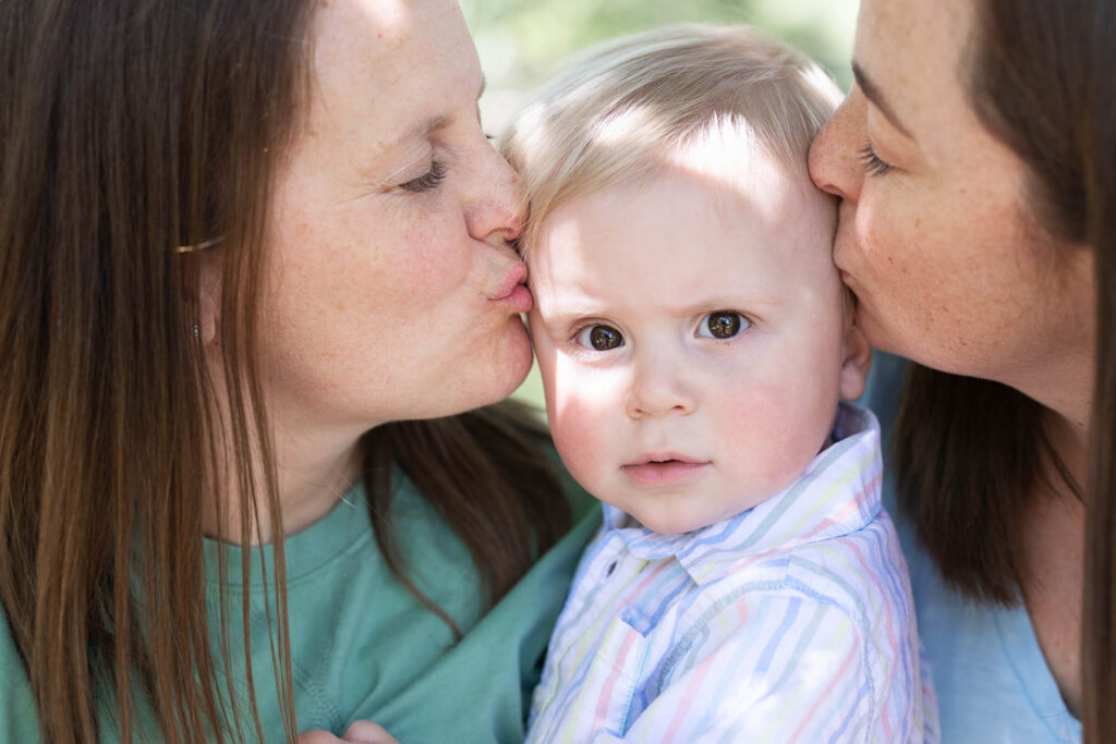 closeup photo of two mothers kissing their baby held between them