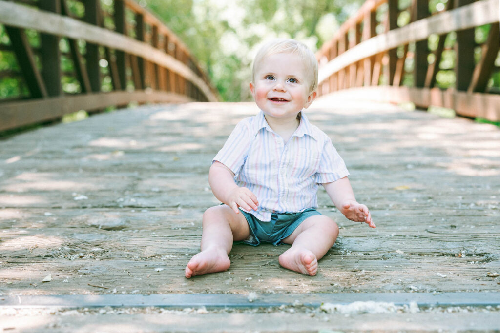 smiling baby sitting on wooden bridge