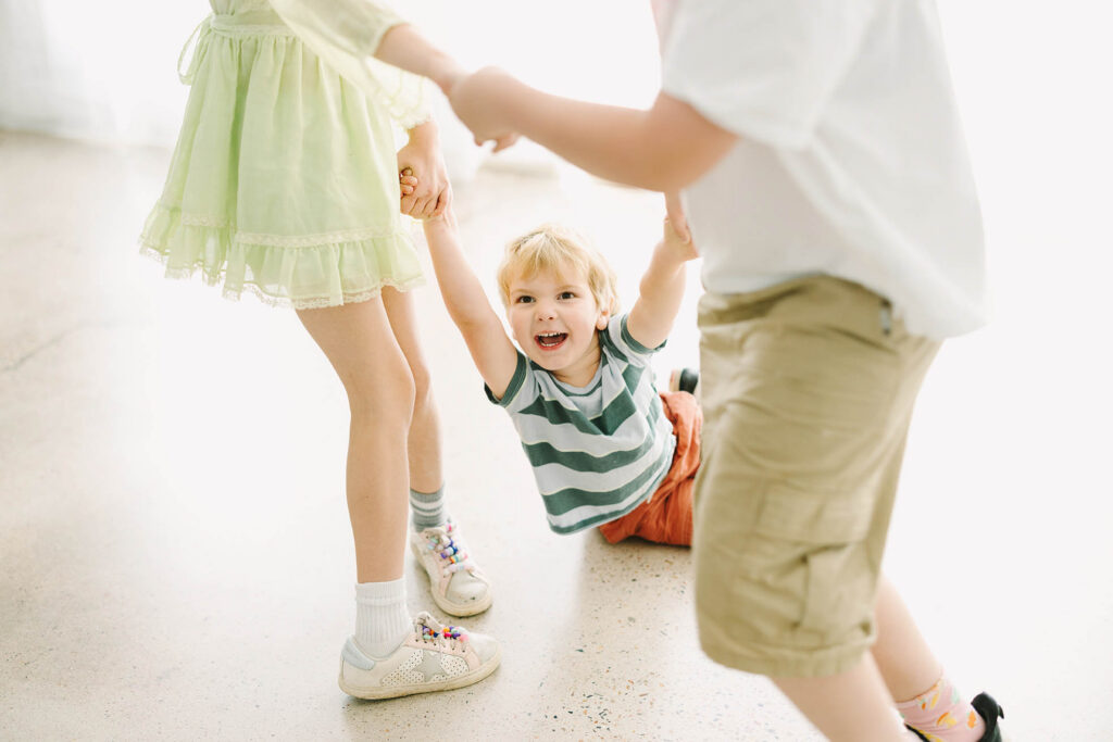 a small boy laughing while be swung by his cousins