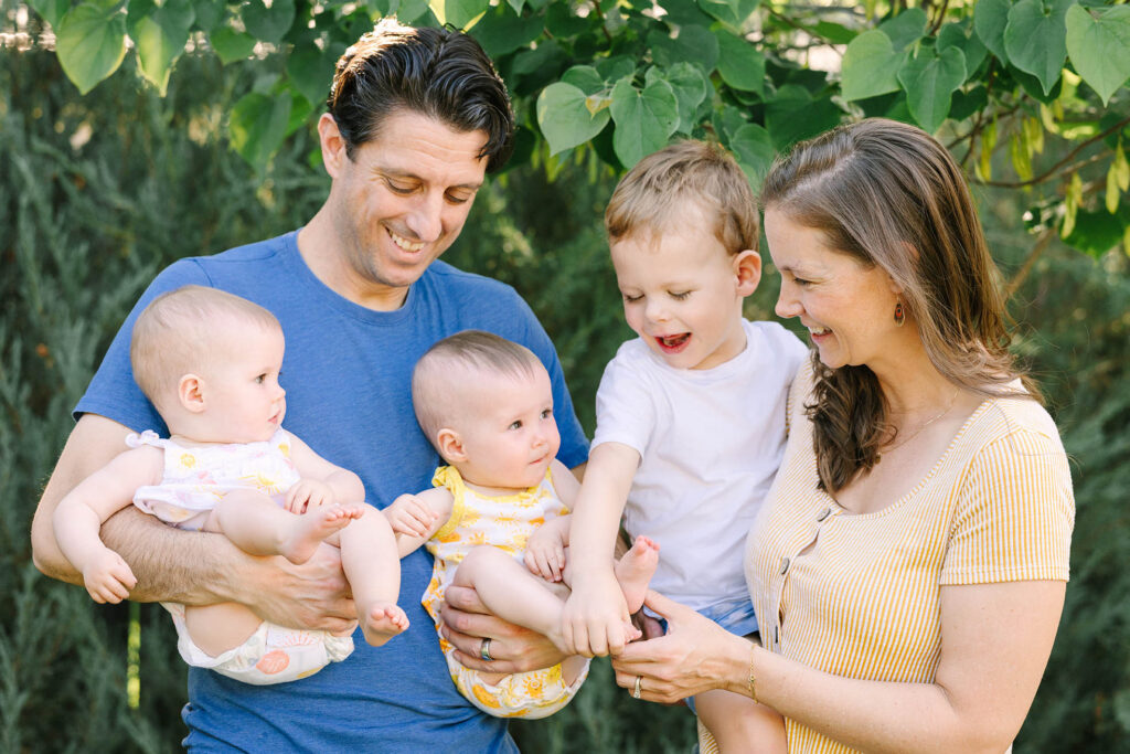 Family of five standing together in lush green backyard, smiling at each other — Fort Collins in-home family photography summer session