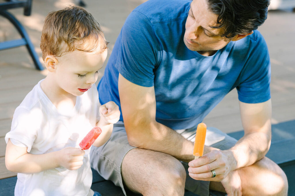 Dad and toddler sharing popsicles on a backyard deck, dappled summer light, Northern Colorado family photography
