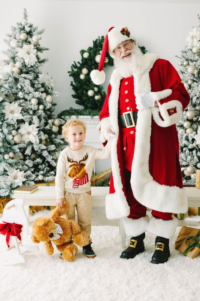 A little boy holding Santa's hand and holding a teddy bear
