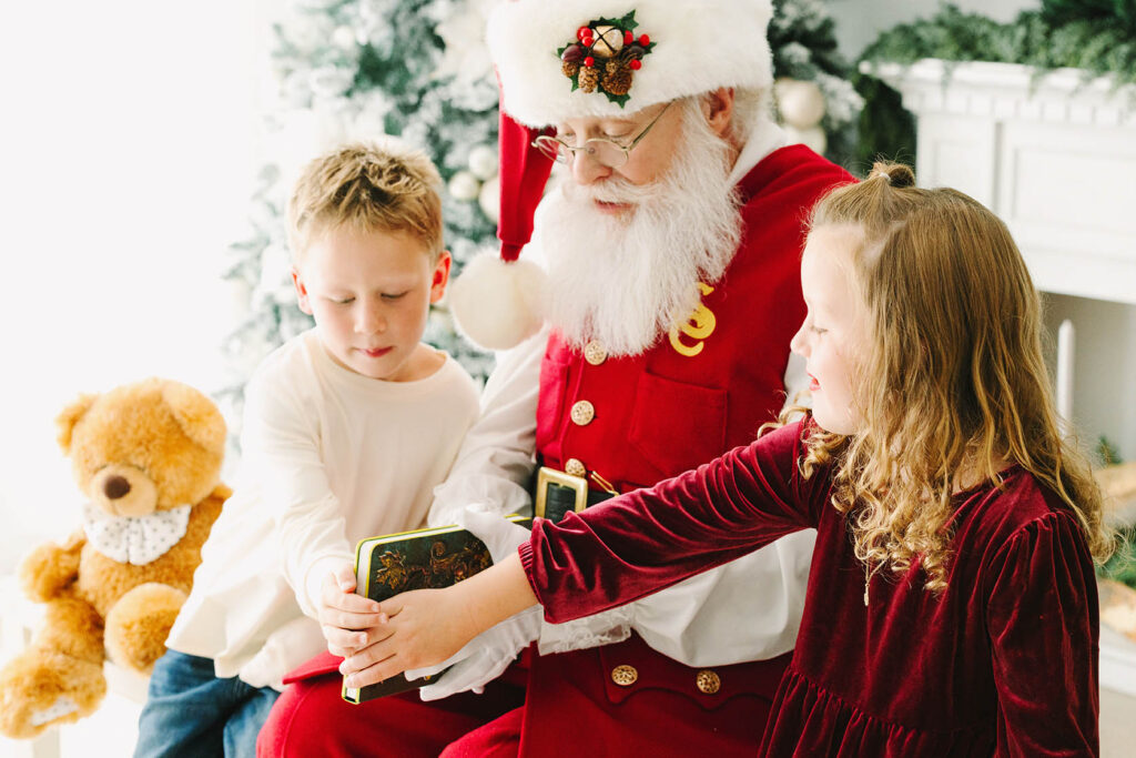 Santa sharing his Nice List book with two siblings